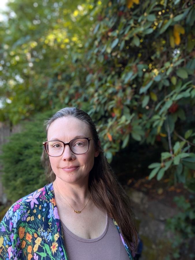 Kristina smiling softly in front of green rhododendron leaves
